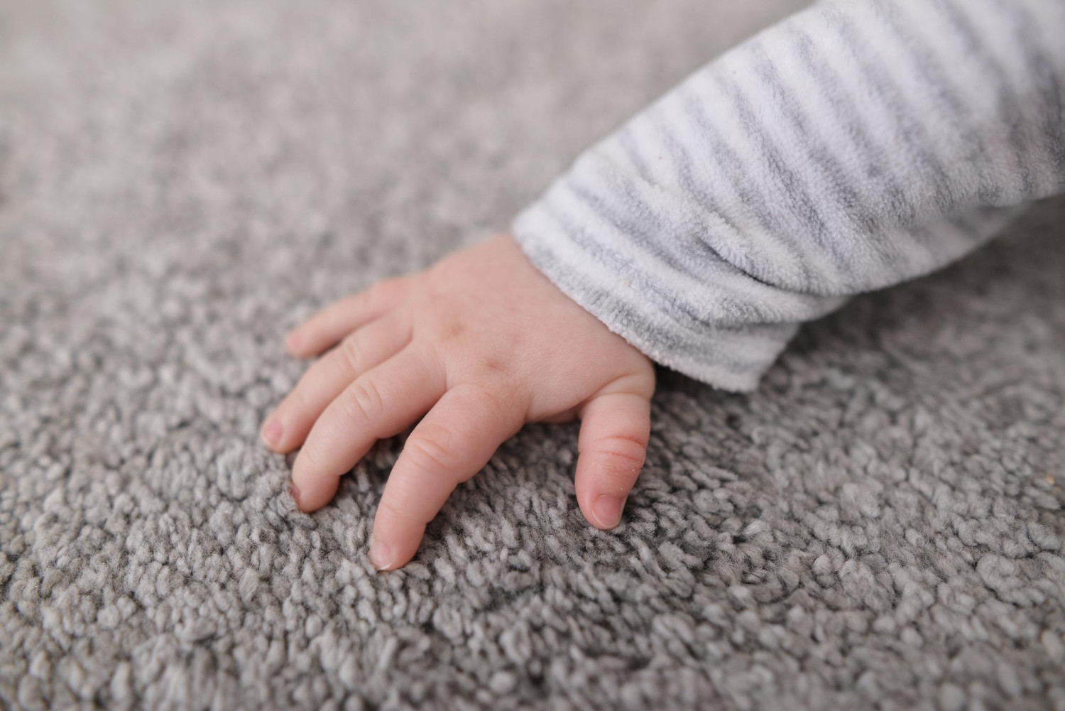 baby hand touching grey new fluffy carpet surface closeup checking softness side view