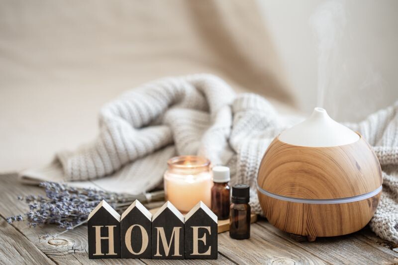 Aroma composition with modern aroma oil diffuser on wooden surface with knitted element, oils and candle on blurred background.