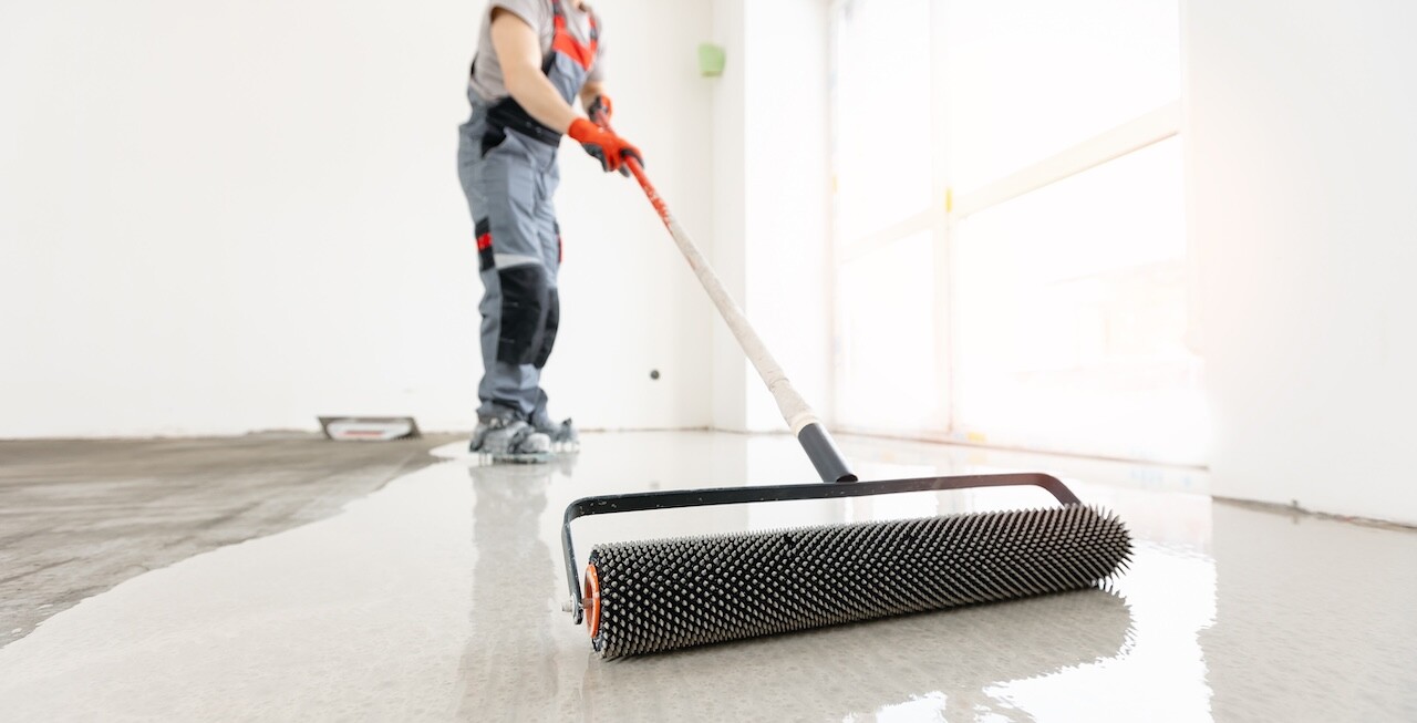 Master with needle roller for new screed concrete with self leveling cement mortar for floors. Concept building renovation home.