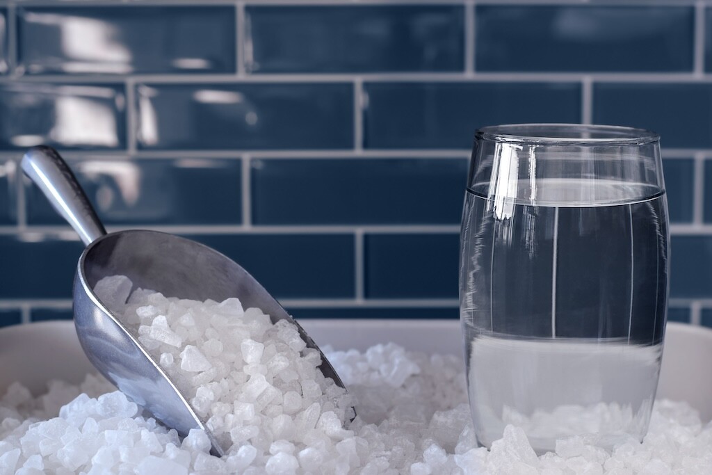 Glass of water and scoop with water softener salt for hard water treatment